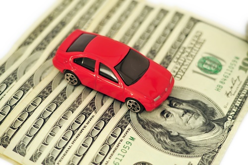 A red toy car drives on top of American dollar bills