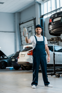 Mechanic standing in a garage full of cars and holding a bottle of motor oil