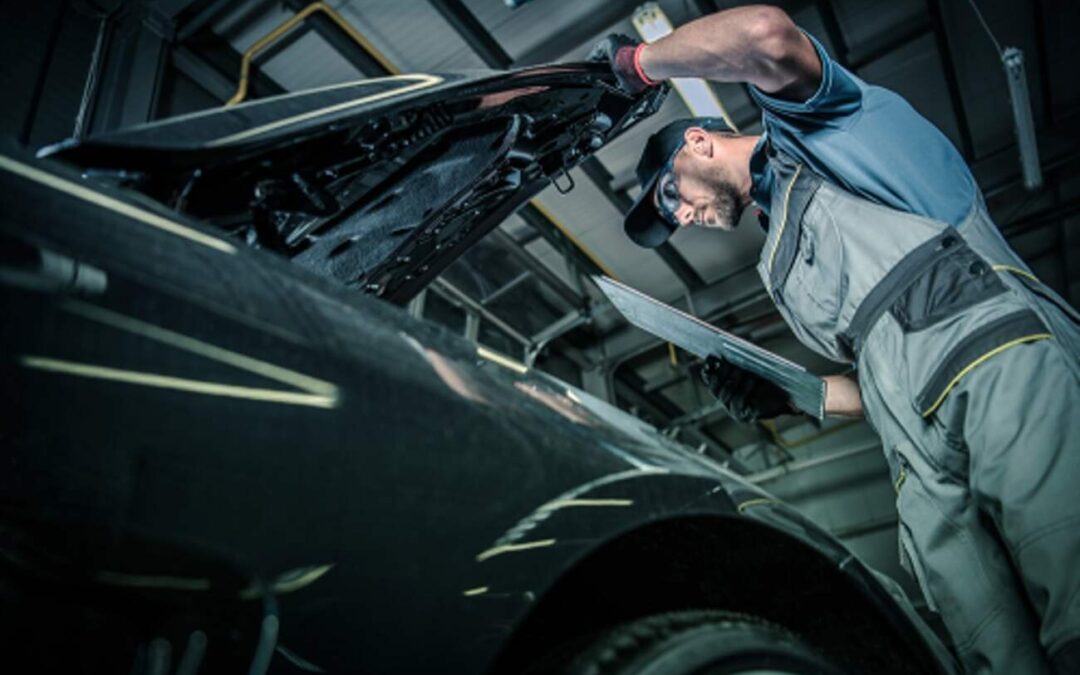 Mechanic inspecting under black vehicle's hood while holding report - Santa Rosa CA
